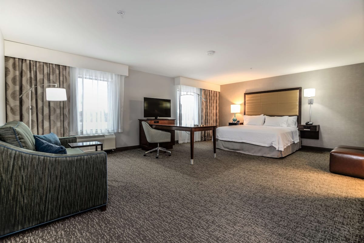 A hotel room with a bed, a desk, a chair, a sofa, and a television.