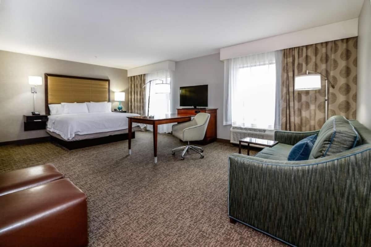A hotel room with a bed, desk, TV, and a sofa.