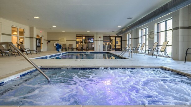A hotel pool area with a hot tub, lounge chairs, and a view of the lobby. - Hampton Inn Brighton (Brighton)