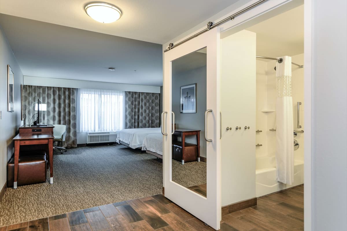 A hotel room with a bed, desk, and a shower area.