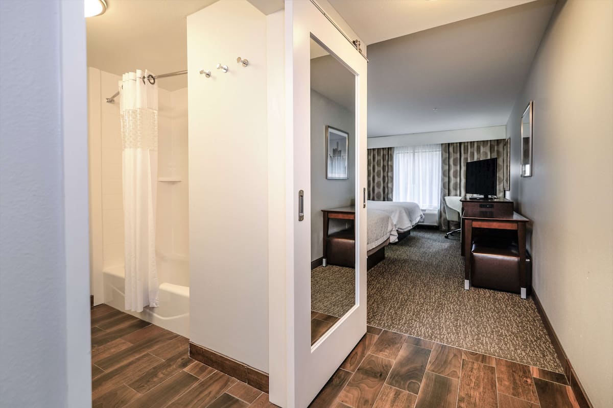 A hotel room with a shower, a bed, a desk, and a mirror.