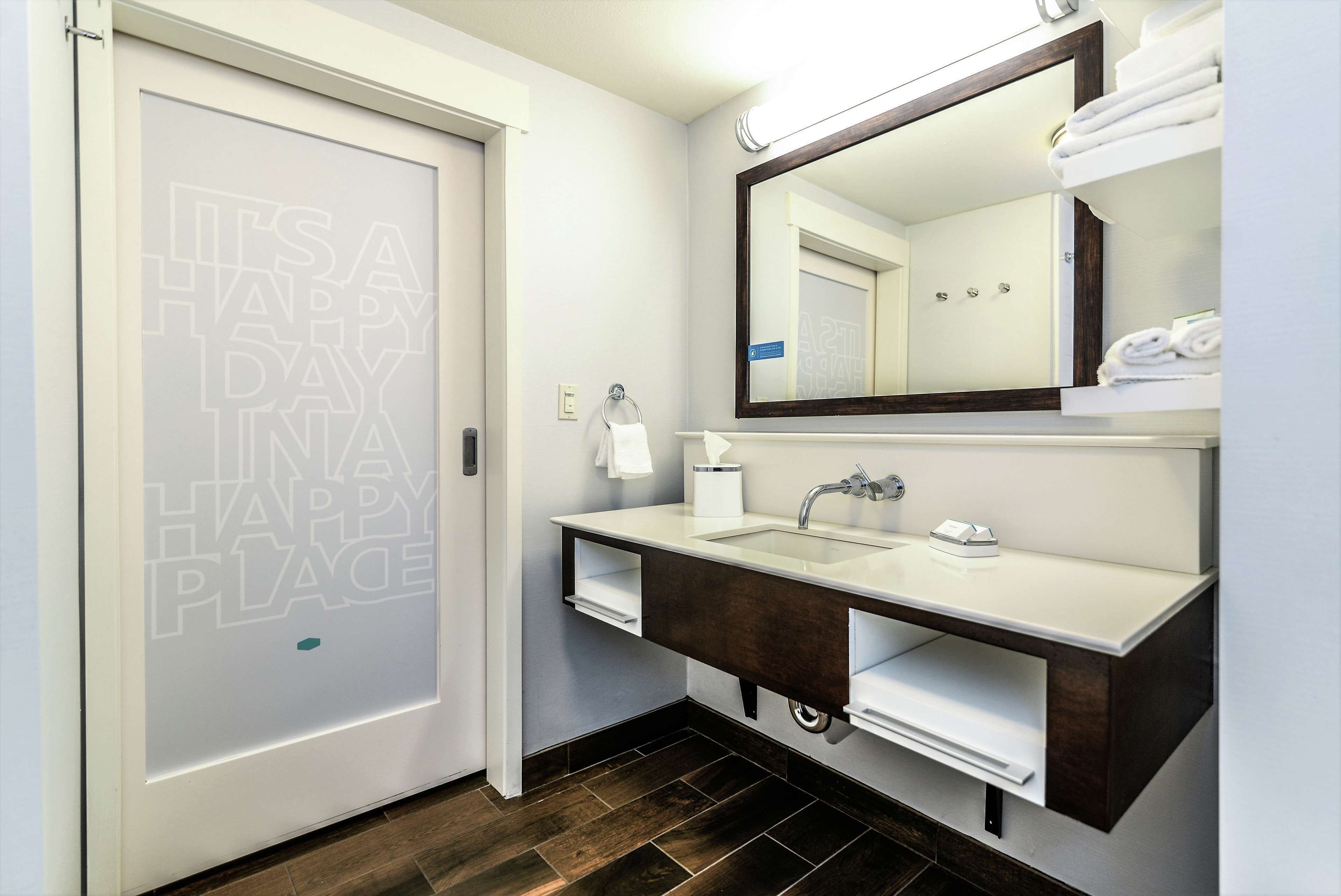 Une salle de bain moderne avec un lavabo blanc, un meuble-lavabo en bois foncé, un grand miroir et un porte-serviettes.