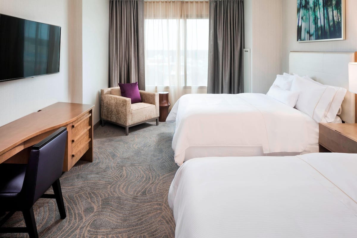A hotel room with a large bed, a smaller bed, a desk, a chair, and a TV.