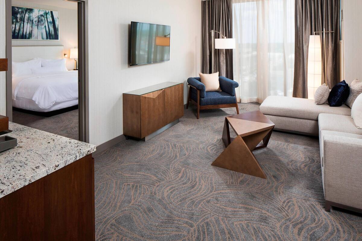 A hotel room with a bed, a sofa, a coffee table, a TV, and a desk.