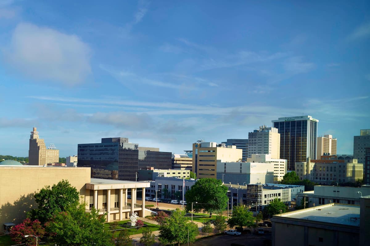 A cityscape with modern buildings, a large open plaza, and a few trees.