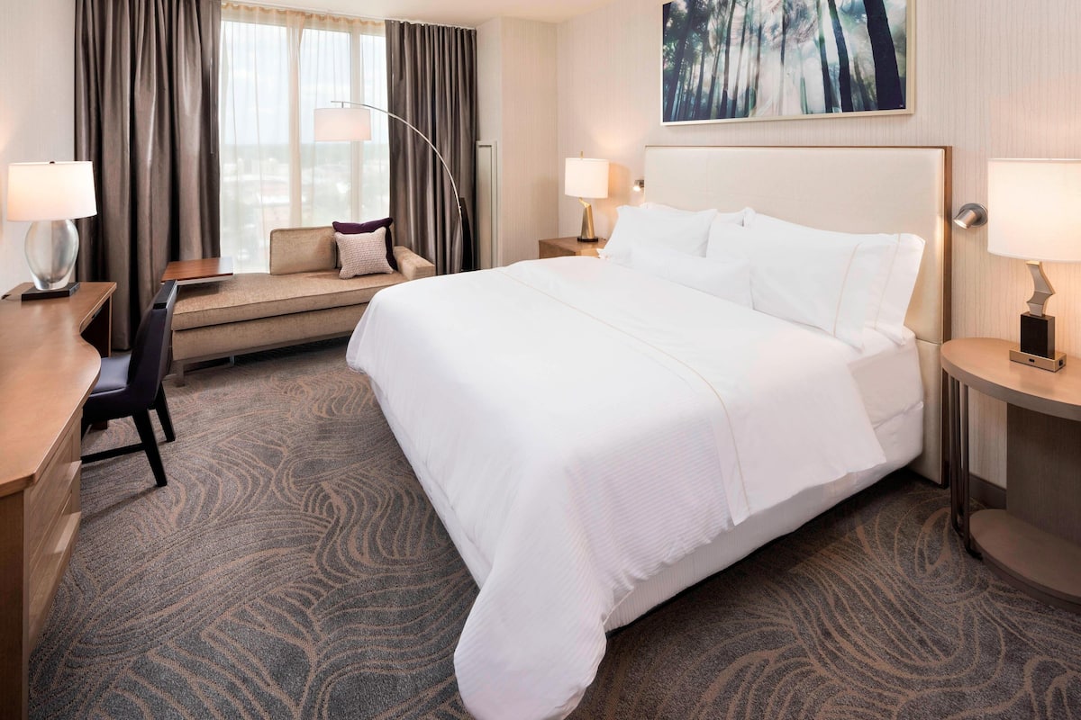 A hotel room with a large bed, a desk, a chair, a sofa, and two bedside tables with lamps.