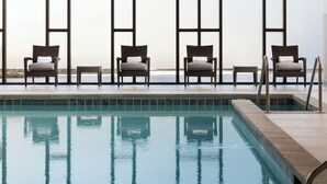 Una piscina con cuatro sillas de mimbre y una mesa pequeña, rodeada de amplios ventanales.