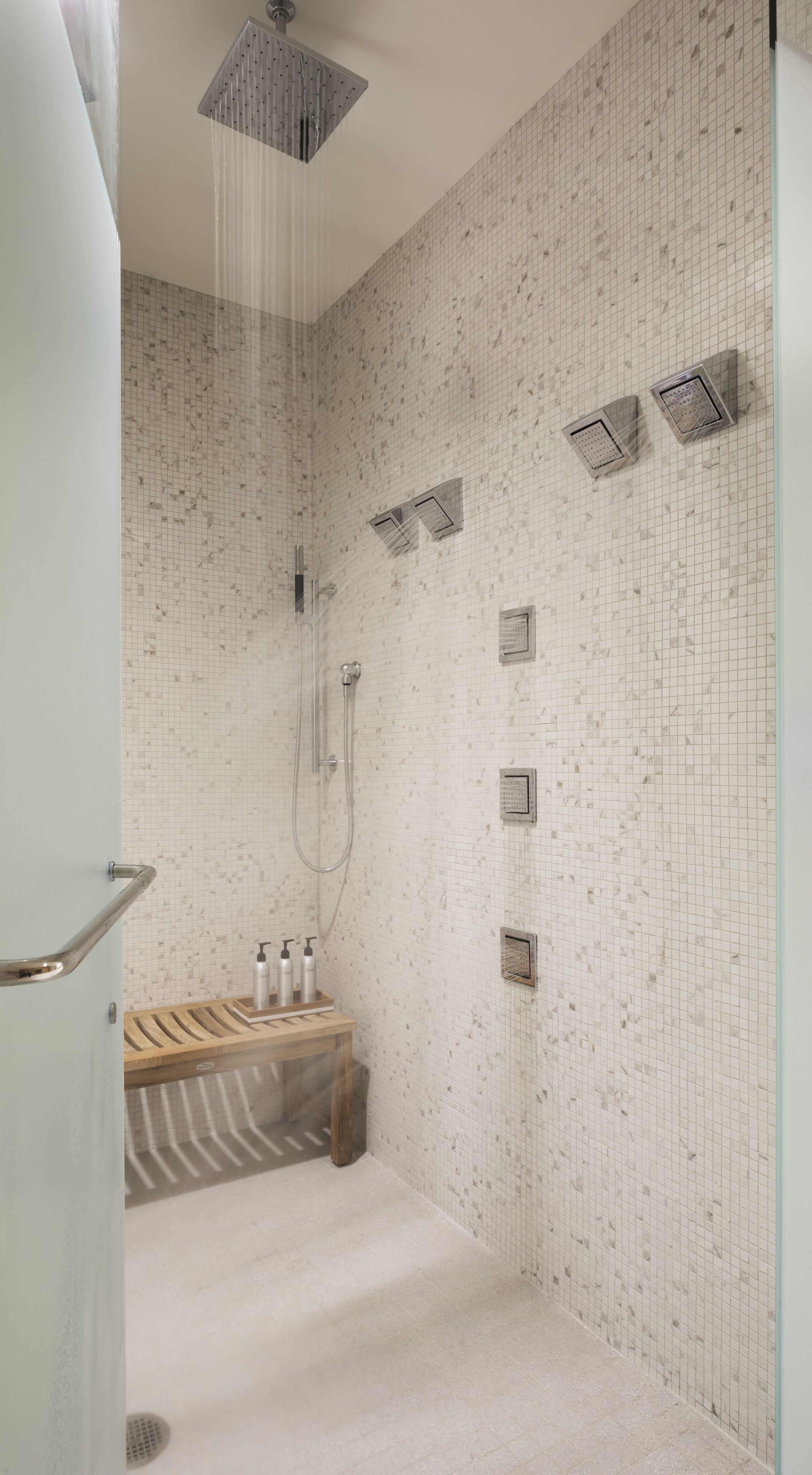A modern bathroom with a shower, a wooden bench, and a tiled wall.