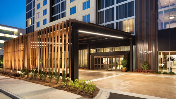 Una entrada de hotel moderna con un vestíbulo cubierto, amplias ventanas y una fachada bien iluminada.