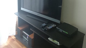 A flat-screen TV on a black entertainment unit with a potted plant, candles, and a framed picture on the wall. - Departamento Belen Marcoleta (Santiago)