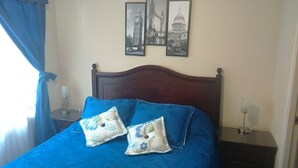 A bed with a blue bedspread and two decorative pillows, a wooden headboard, and two framed pictures on the wall. - Departamento Belen Marcoleta (Santiago)