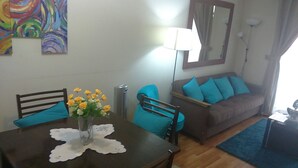 A dining area with a table, chairs, and a vase of flowers. There is a sofa with blue cushions and a mirror on the wall. - Departamento Belen Marcoleta (Santiago)