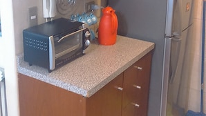 A compact kitchen with wooden cabinets, a microwave, a toaster, and a refrigerator. - Departamento Belen Marcoleta (Santiago)