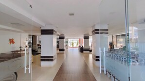Ein moderner Hotelkorridor mit Glastrennwänden, einem Empfangstresen und Blick ins Freie.
