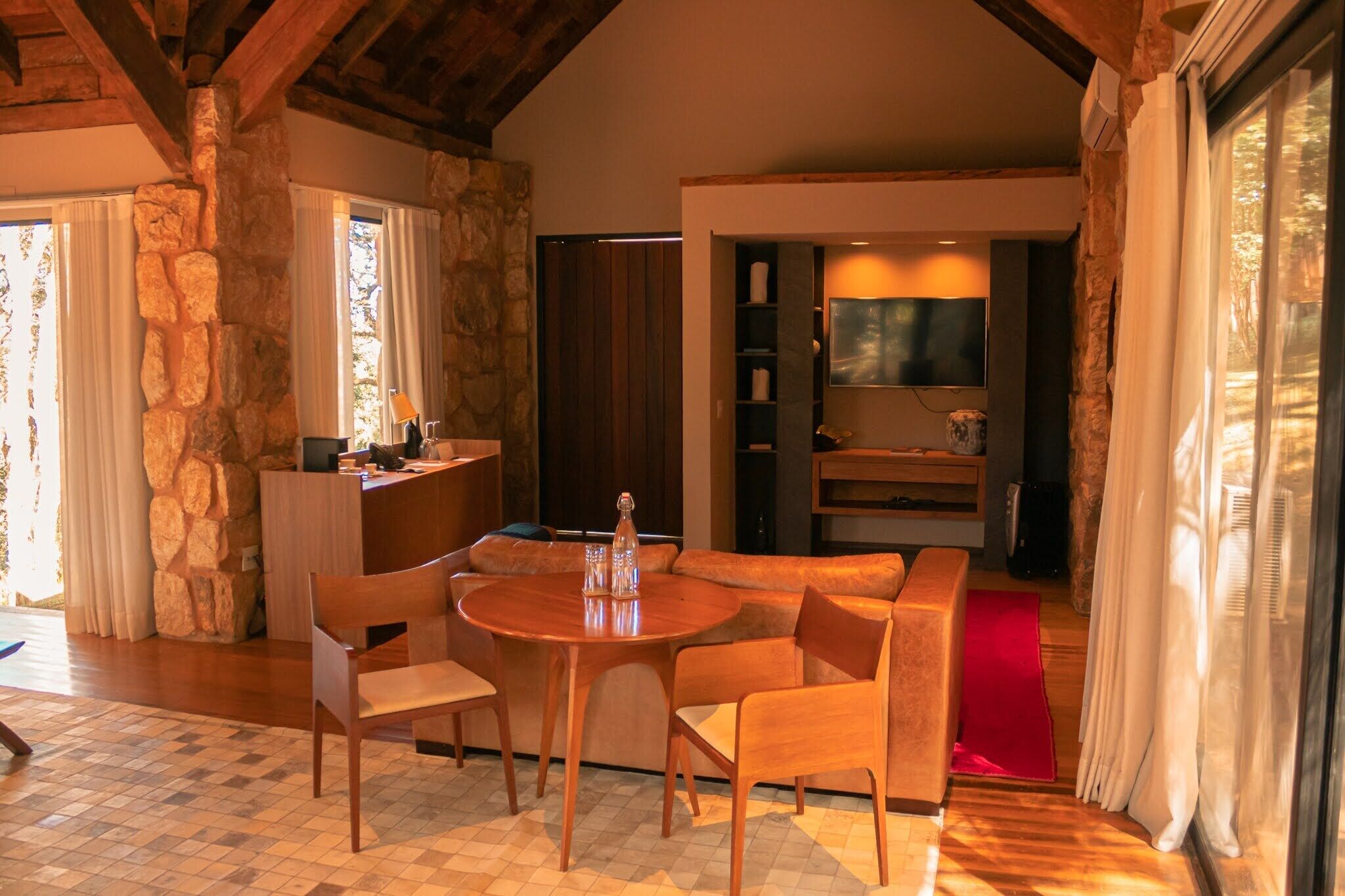Una habitación acogedora con pared de piedra, una mesa de comedor de madera con sillas, un sofá y un televisor fijado a la pared.