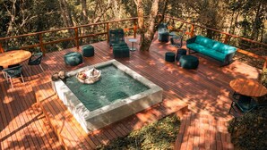 Eine Terrasse mit Whirlpool, Sitzgelegenheiten und Blick auf den Wald.