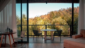 Ein modernes Wohnzimmer mit einem großen Schiebeglasfenster, das auf einen Balkon mit Blick auf einen Wald führt.