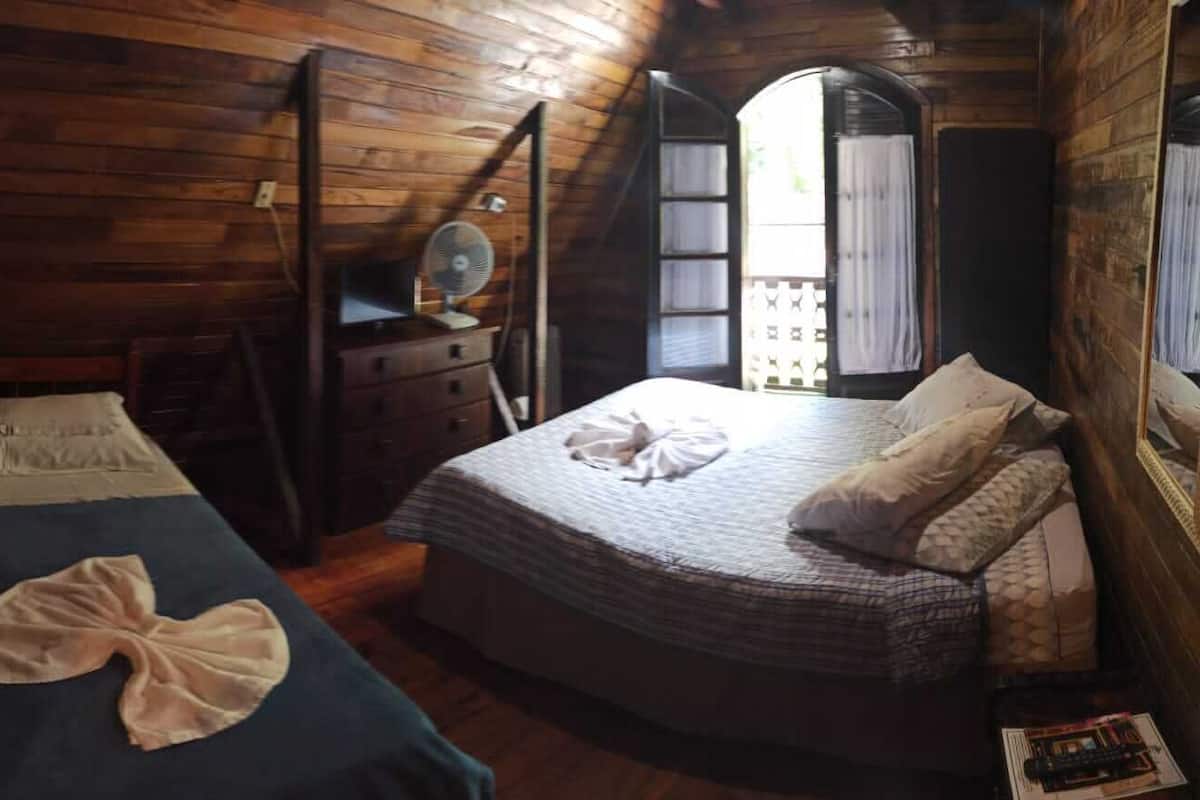A wooden cabin room with two beds, a desk, and a mirror.