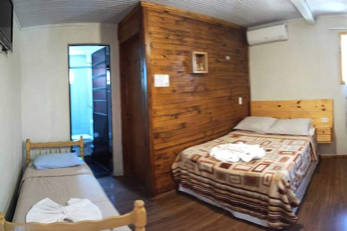 A room with a wooden wall, a bed with a patterned blanket, a bedside table, and a small chair.