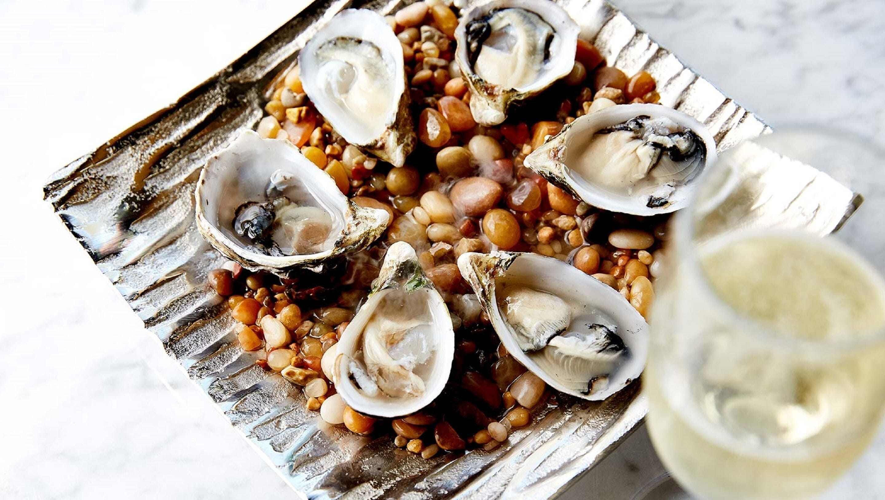 Un plato de ostras, frijoles y una copa de vino blanco.