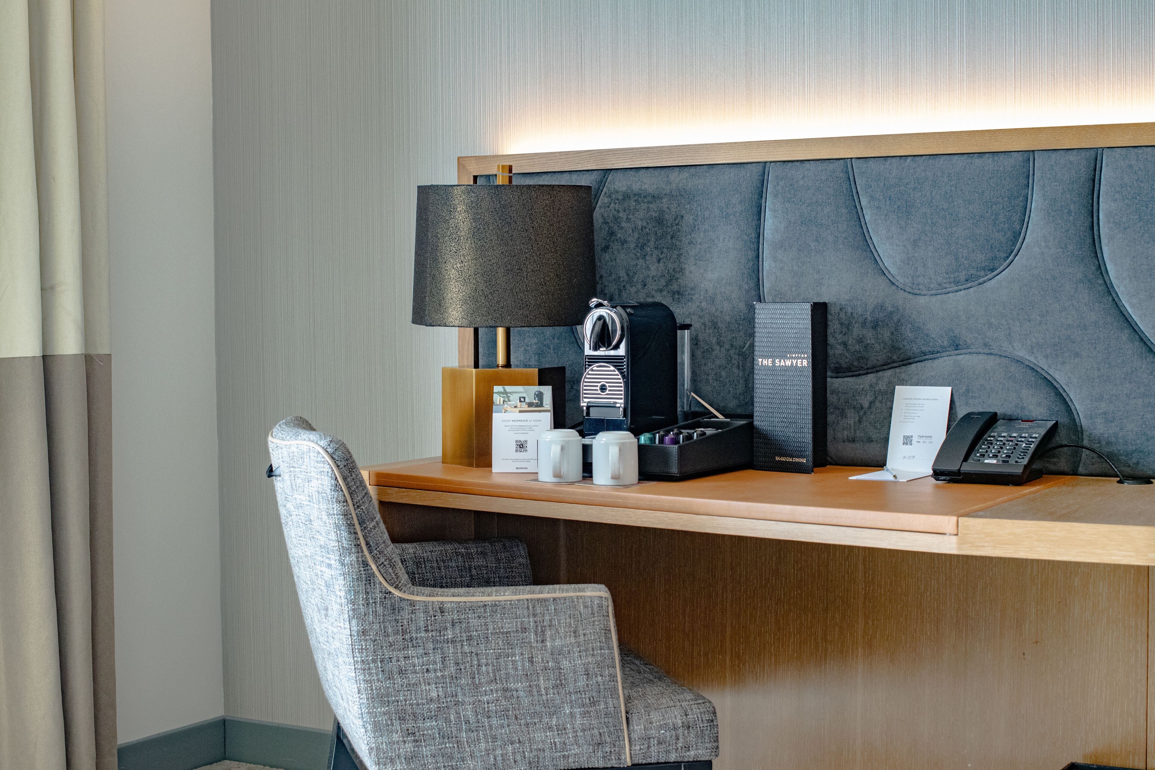 Un bureau d’hôtel avec une lampe, un téléphone, une machine à café et une valise.