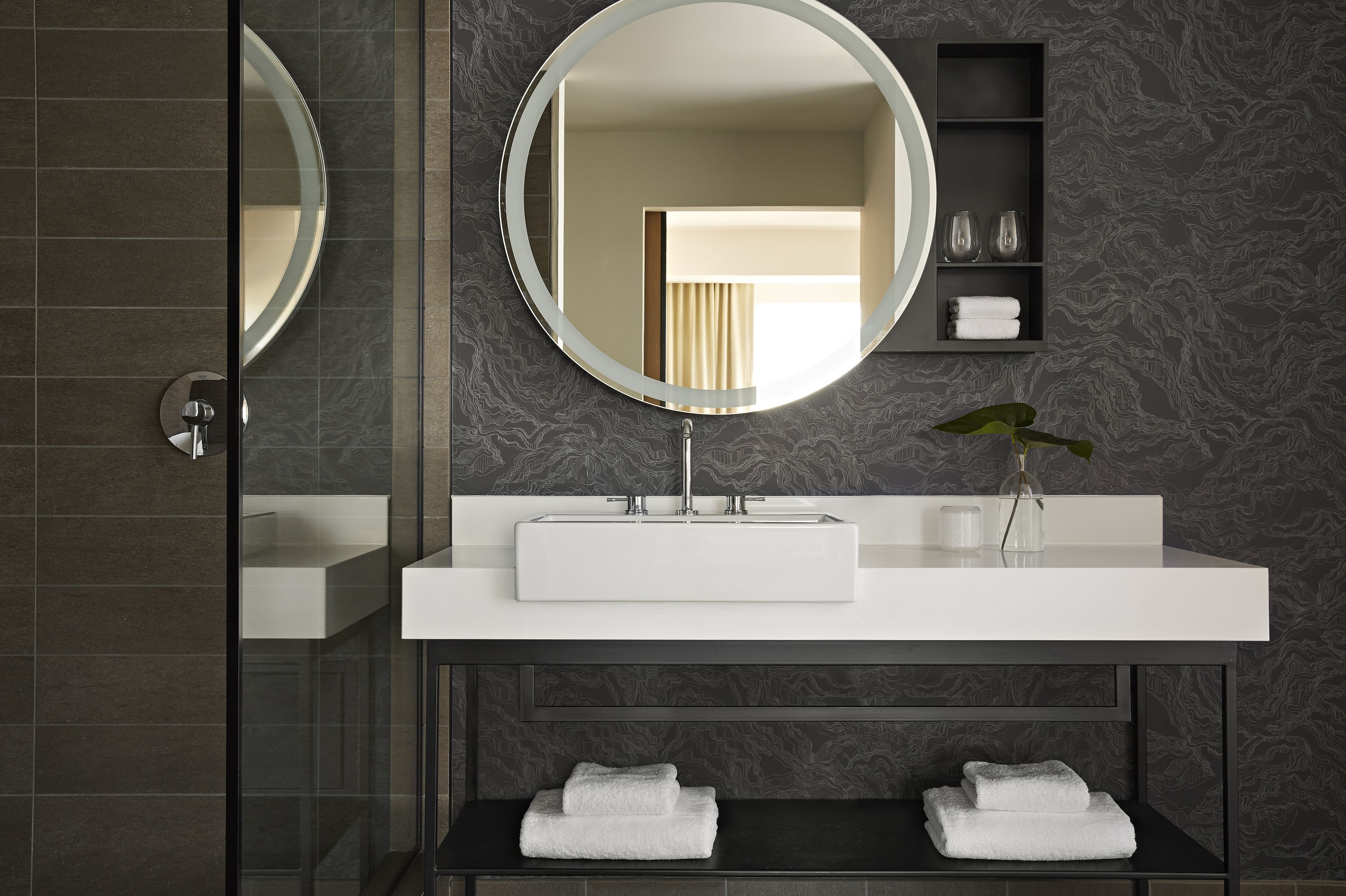 A modern bathroom with a large mirror, white sink, and dark patterned walls.