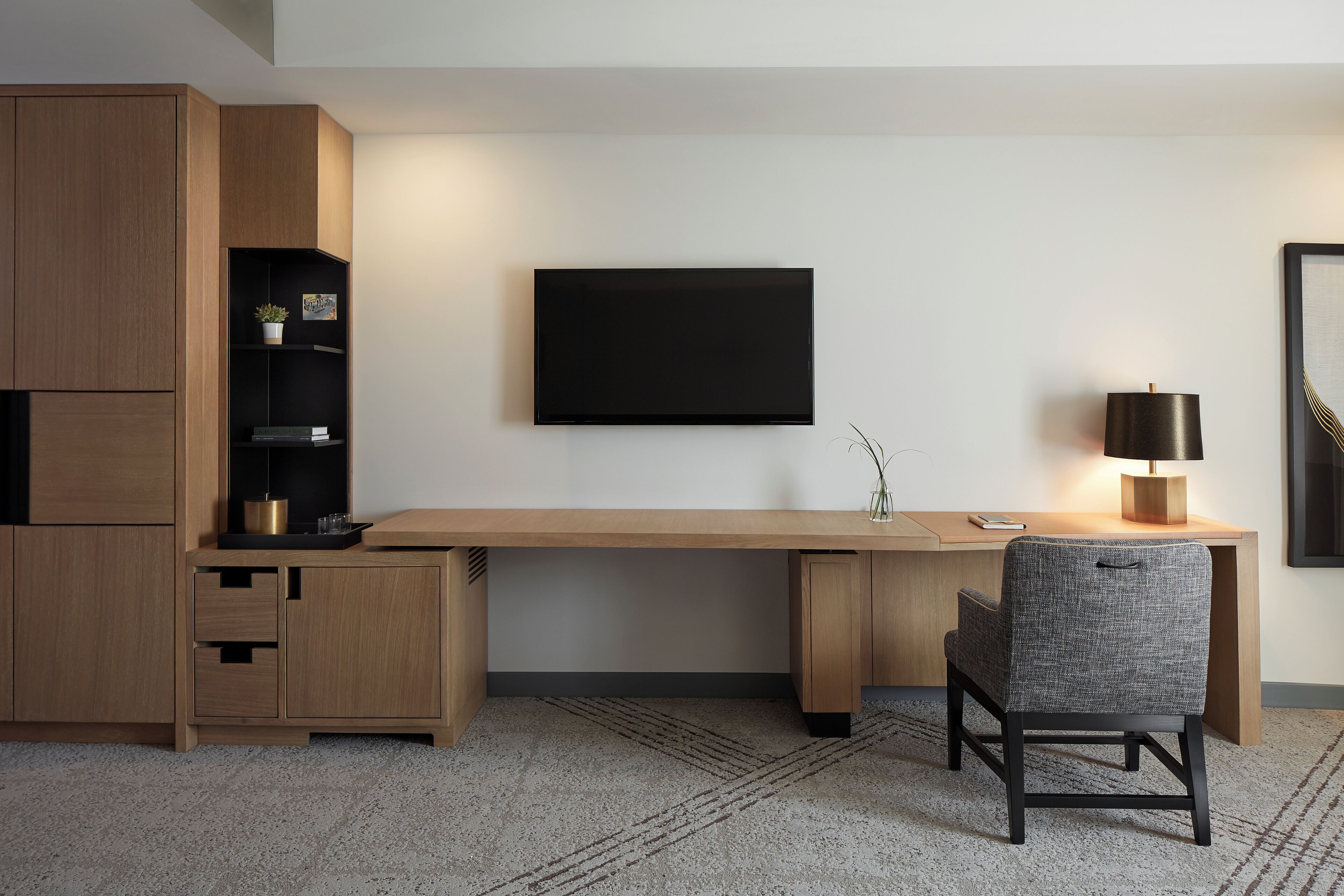 A modern room with a wooden desk, a flat-screen TV, a chair, and a lamp.