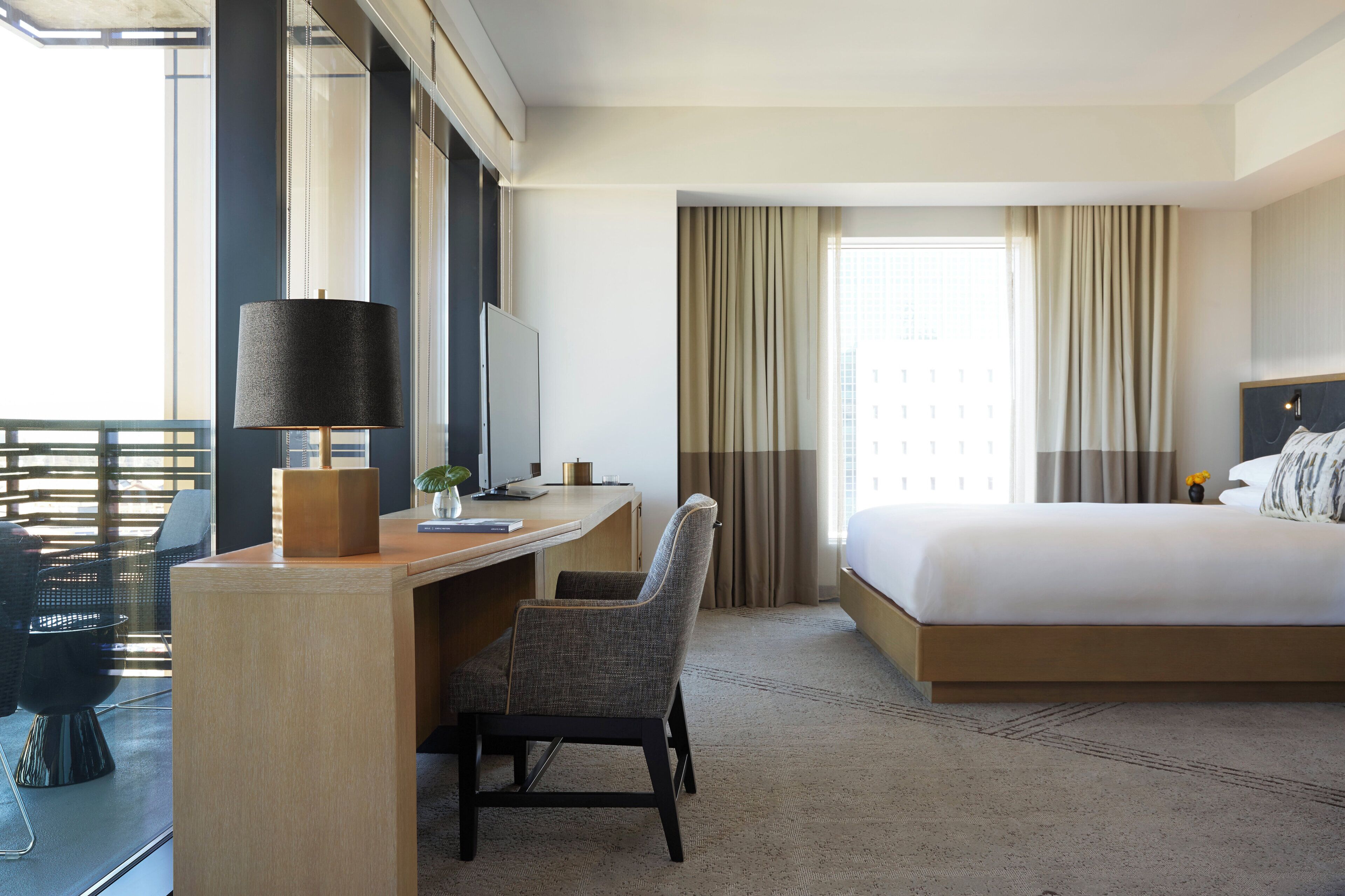Habitación de hotel con cama, escritorio, silla y un amplio ventanal con cortinas.