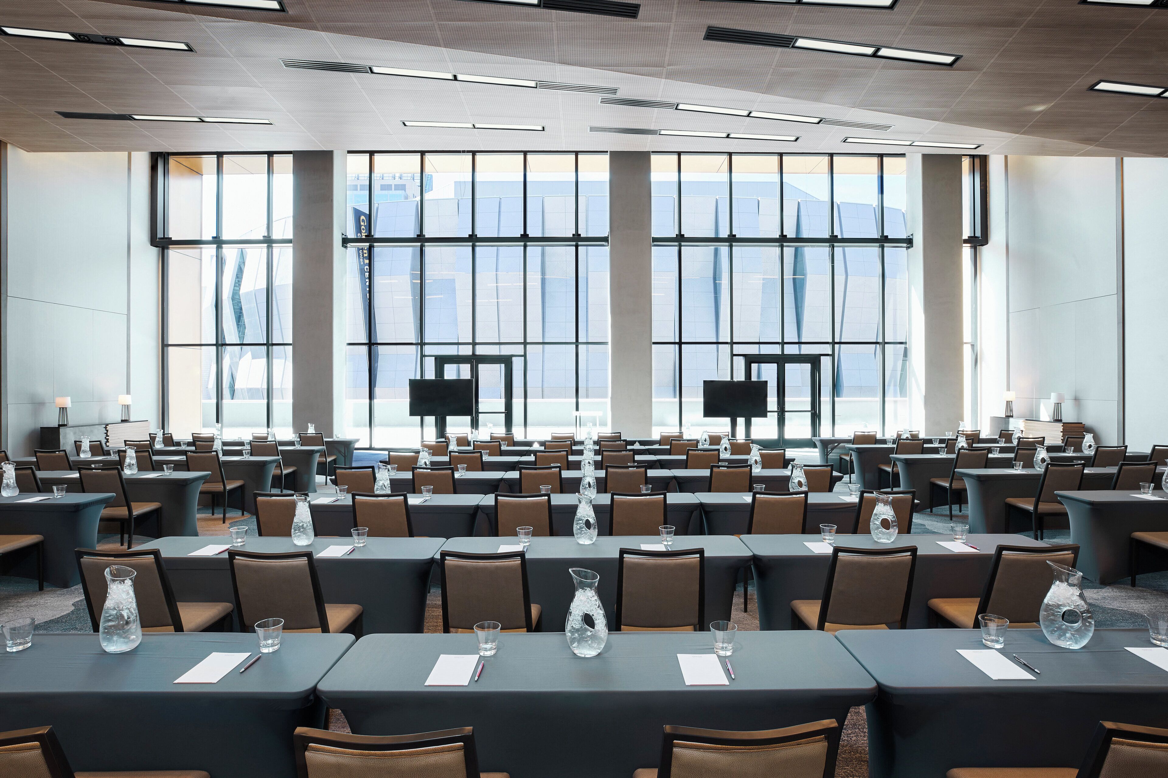 A conference room with multiple tables and chairs, large windows, and a modern ceiling design.