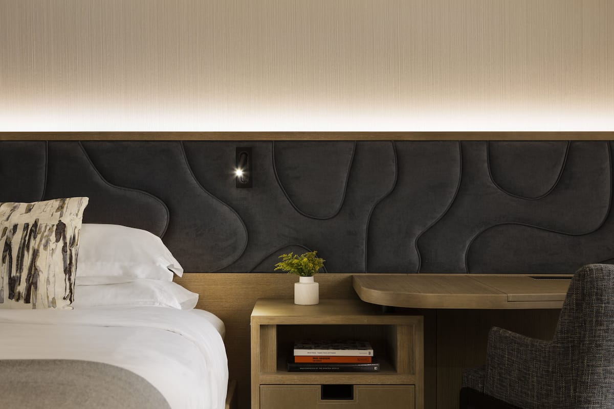 Une chambre d’hôtel moderne avec un lit bien fait, une table de chevet agrémentée d’une plante et une petite bibliothèque.