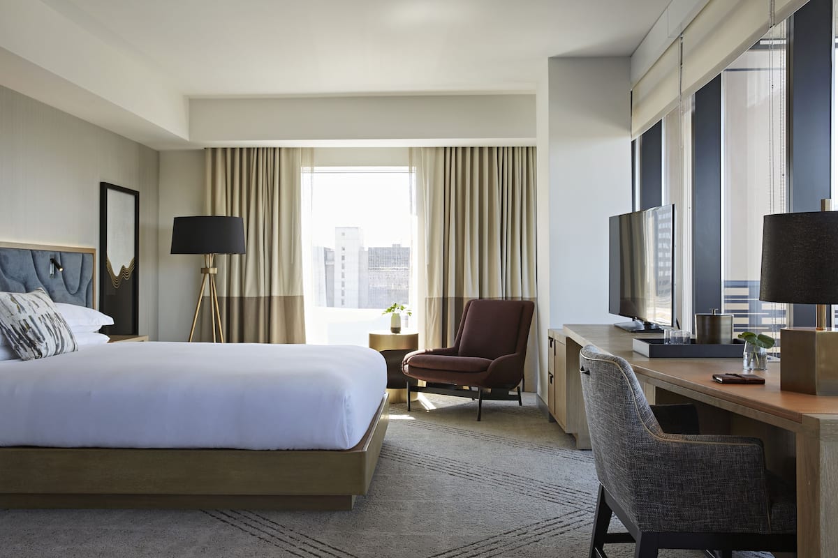 Une chambre d’hôtel avec un grand lit, un bureau, une chaise, une télévision et une fenêtre avec des rideaux.