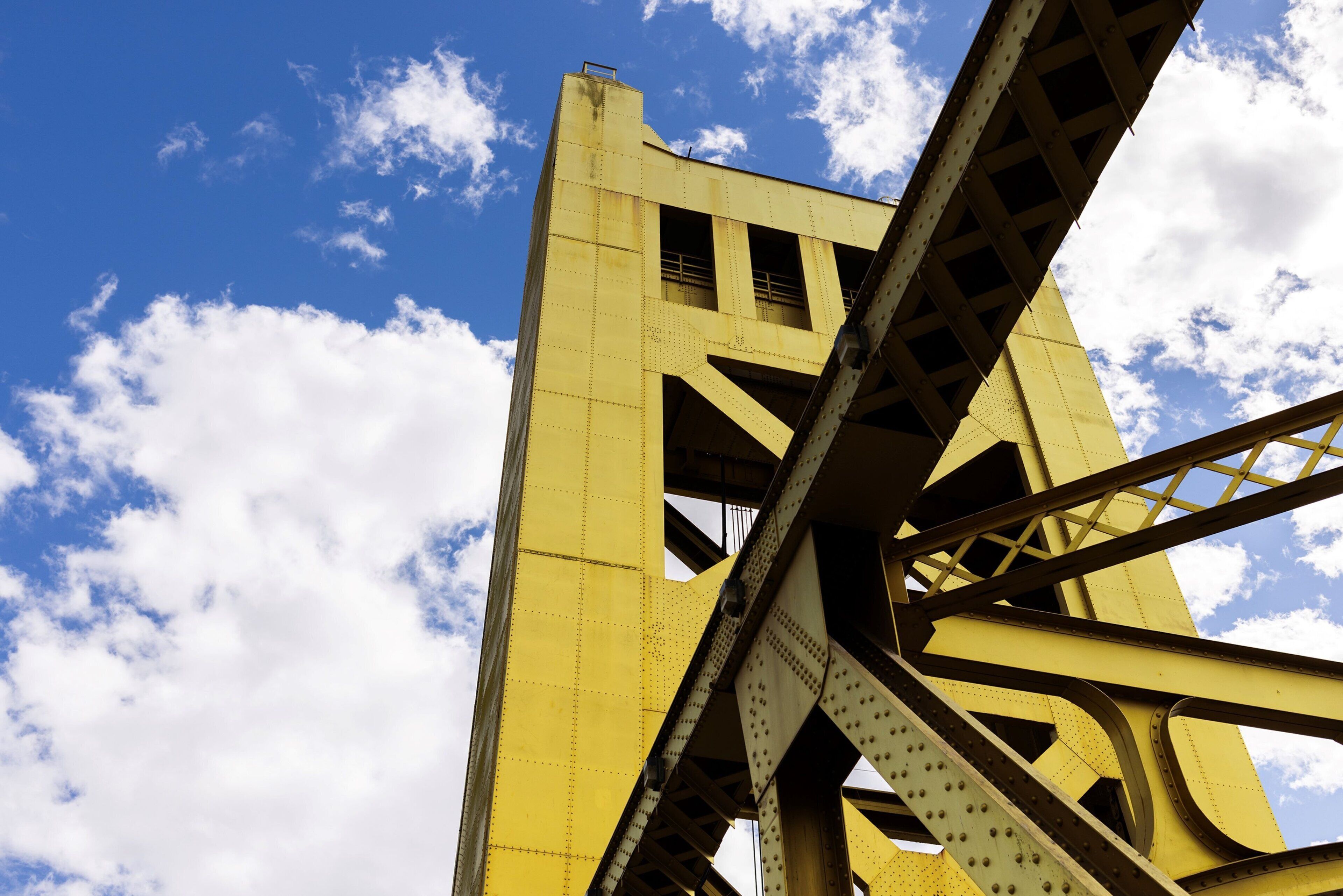 A large yellow bridge structure against a blue sky with clouds.
