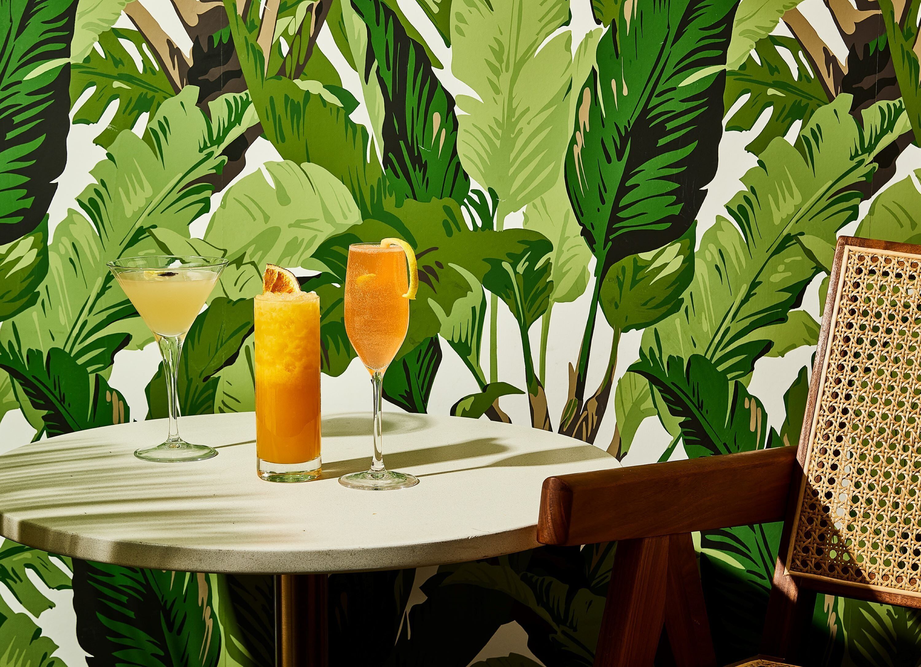 Een ronde tafel met twee drankjes en een rieten stoel.
