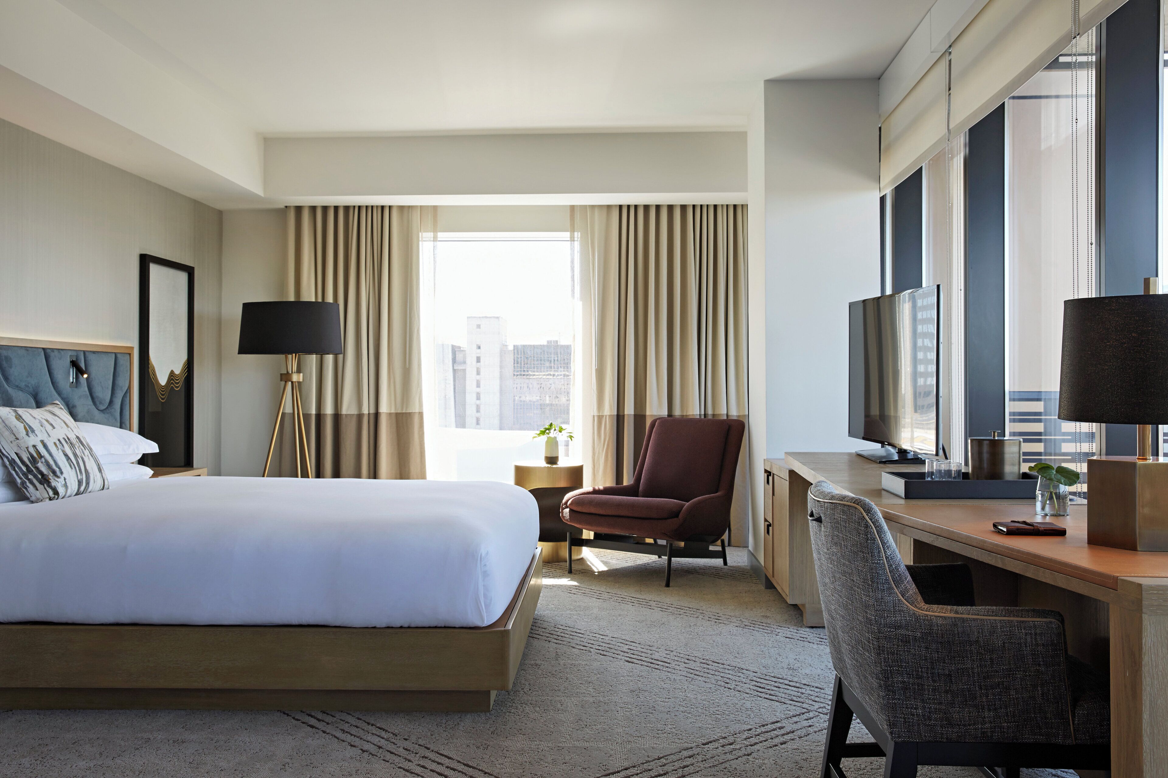 A hotel room with a bed, a desk, a chair, a TV, and a window with curtains.