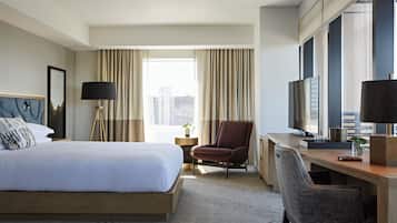 A hotel room with a bed, a desk, a chair, a TV, and a window with curtains.