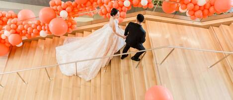 Una pareja de novios baja por una escalera de madera adornada con globos naranja y blancos.