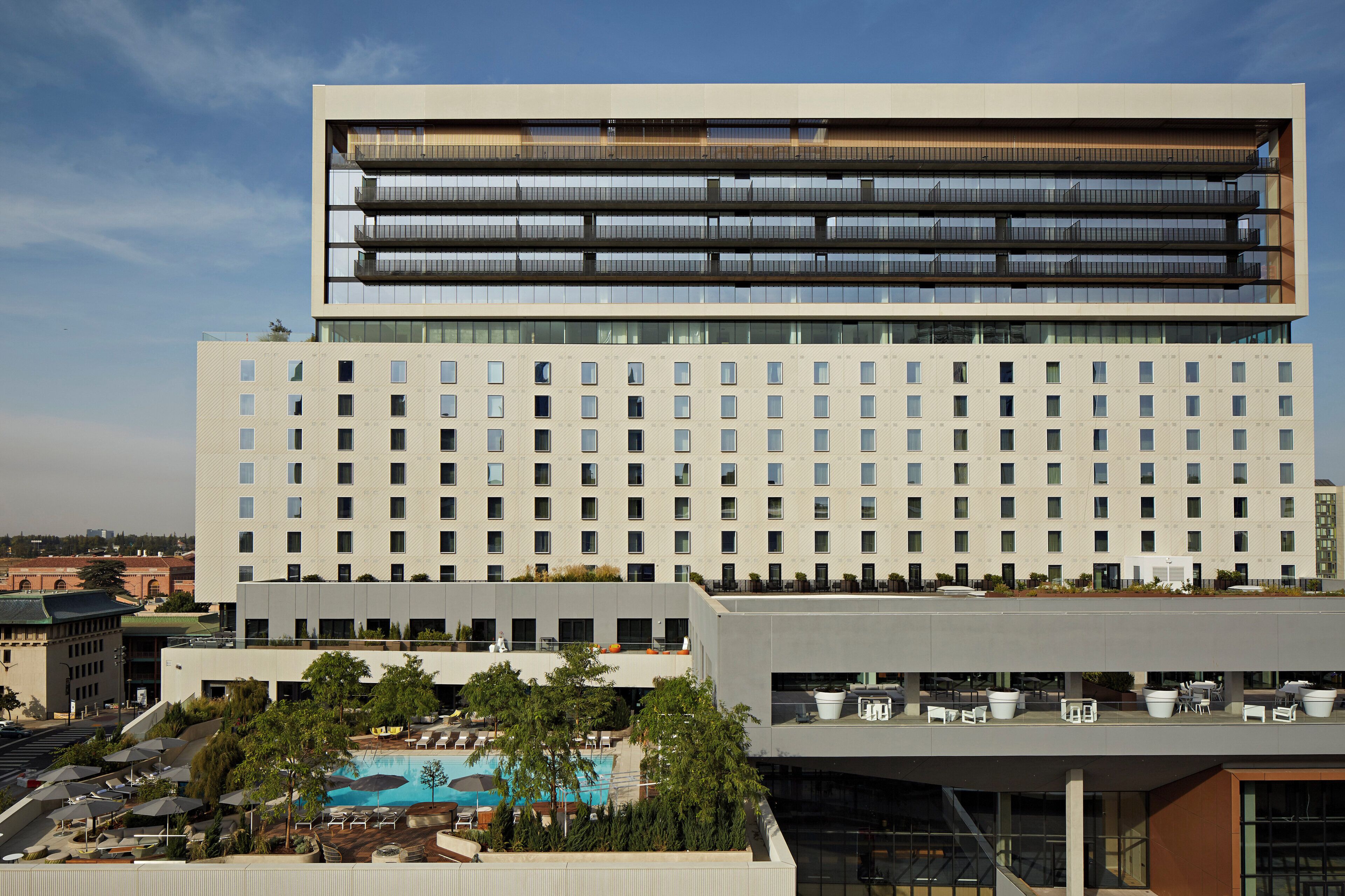 Een modern hotel met een zwembad op het dak, meerdere balkons en een grote glazen gevel.