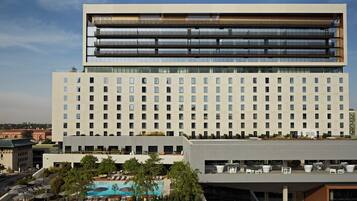 Een modern hotel met een zwembad op het dak, meerdere balkons en een grote glazen gevel.