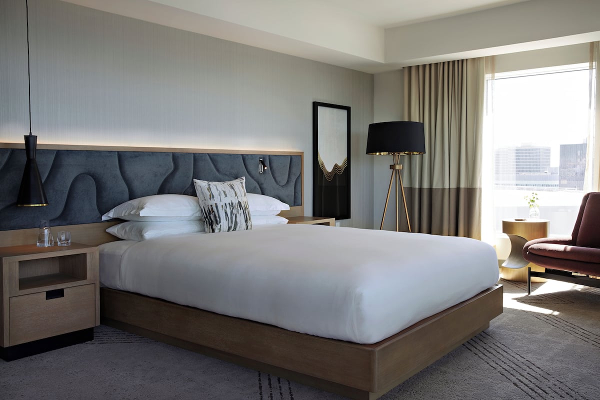 Une chambre d’hôtel moderne avec un grand lit, une table de chevet, une lampe, une chaise et une vue sur la ville.