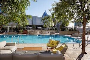 Un área de piscina con sillones de descanso y sombrillas, rodeada de árboles y edificios.
