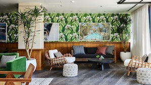 A modern living room with a wooden panel wall, green and white furniture, and large tropical plant decorations. - Kimpton Sawyer Hotel by IHG (Sacramento)