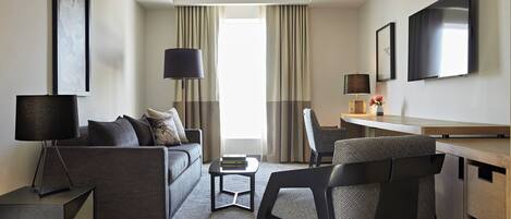 Habitación de hotel moderna con sofá, sillón, escritorio y televisor de pantalla plana.
