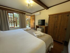 Quarto de hotel com uma cama grande, uma televisão sobre um suporte de madeira, um guarda-roupa e uma janela com cortinas.