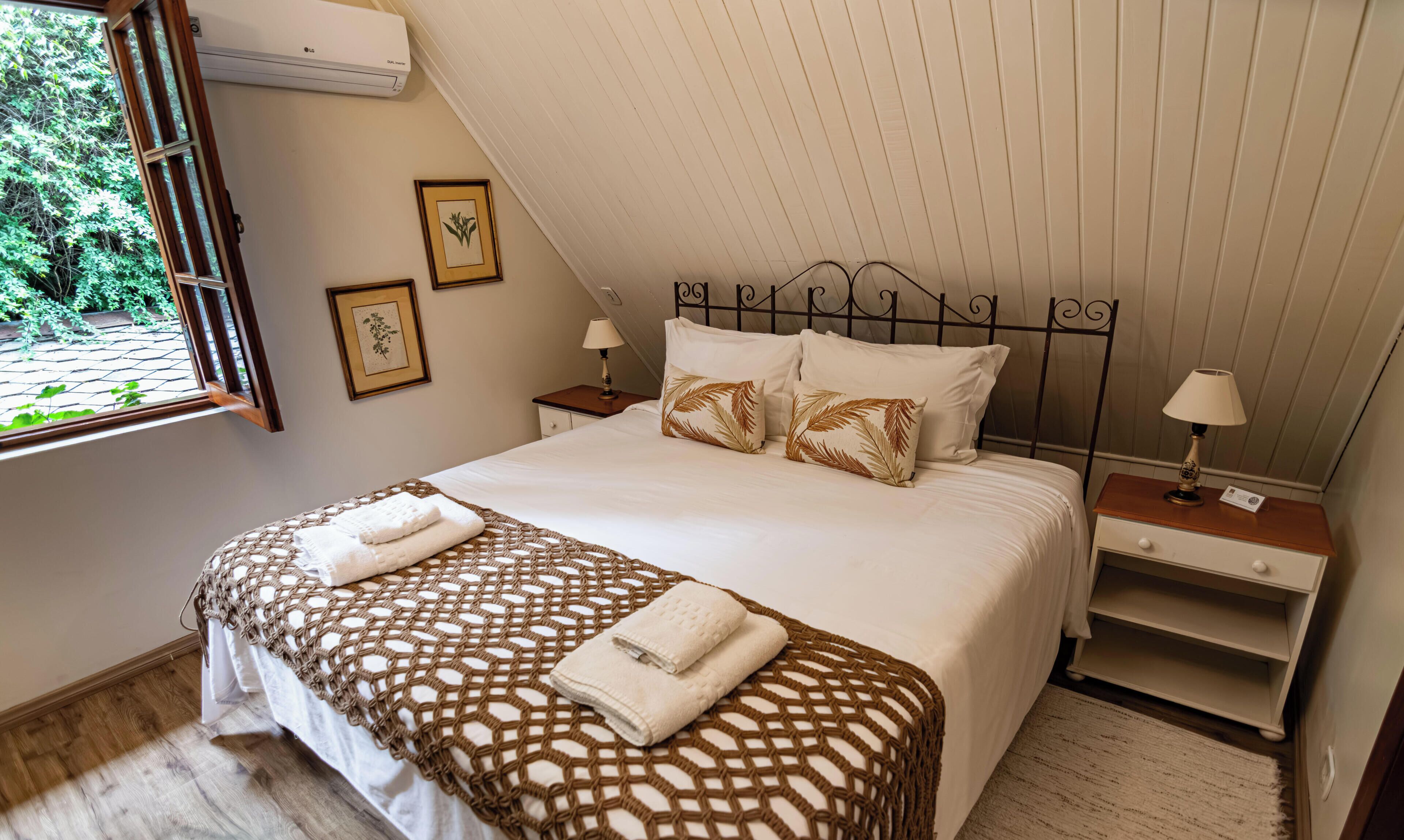 A bedroom with a bed, two bedside tables, a window, and a wall-mounted air conditioner.