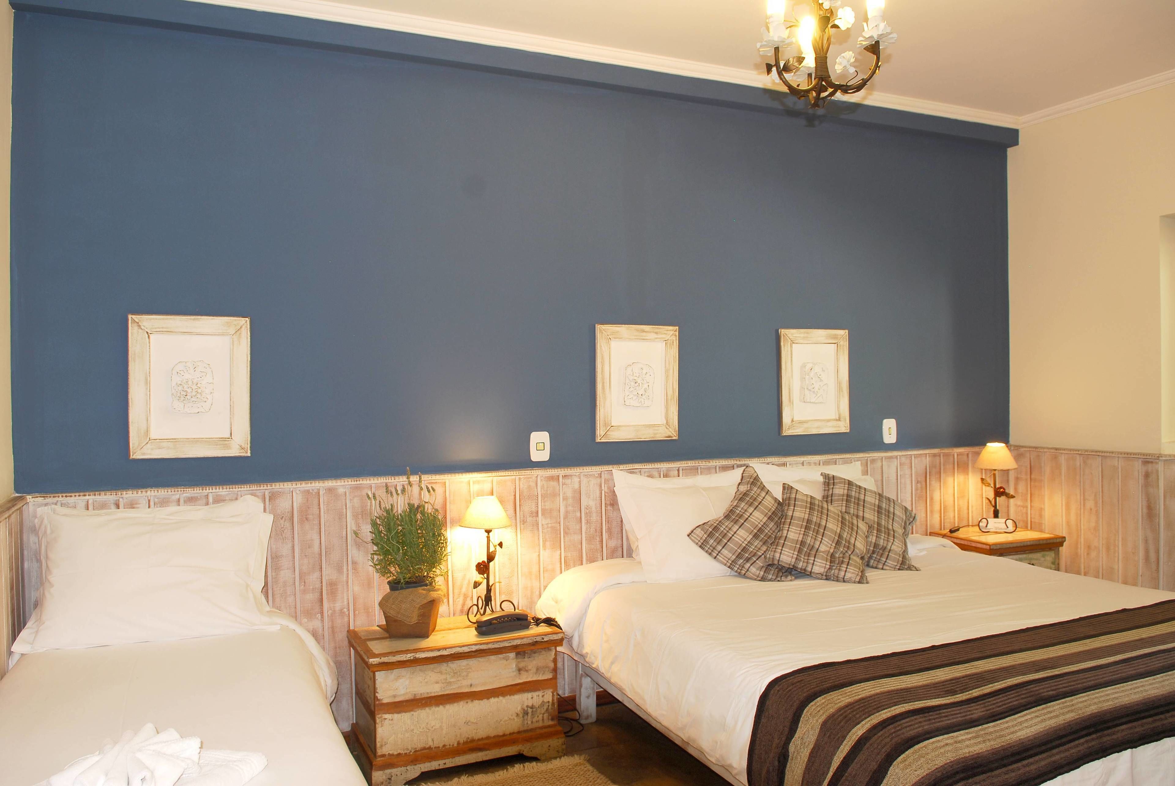 A double room with two beds, a wooden headboard, bedside tables with lamps, and framed pictures on the wall.