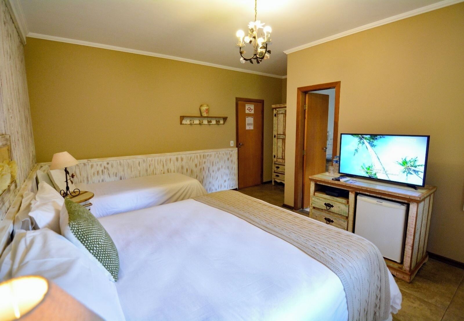 Ein Hotelzimmer mit zwei Betten, einem Fernseher auf einem Holzständer, einem kleinen Tisch mit einer Lampe und einer Tür zu einem Badezimmer.