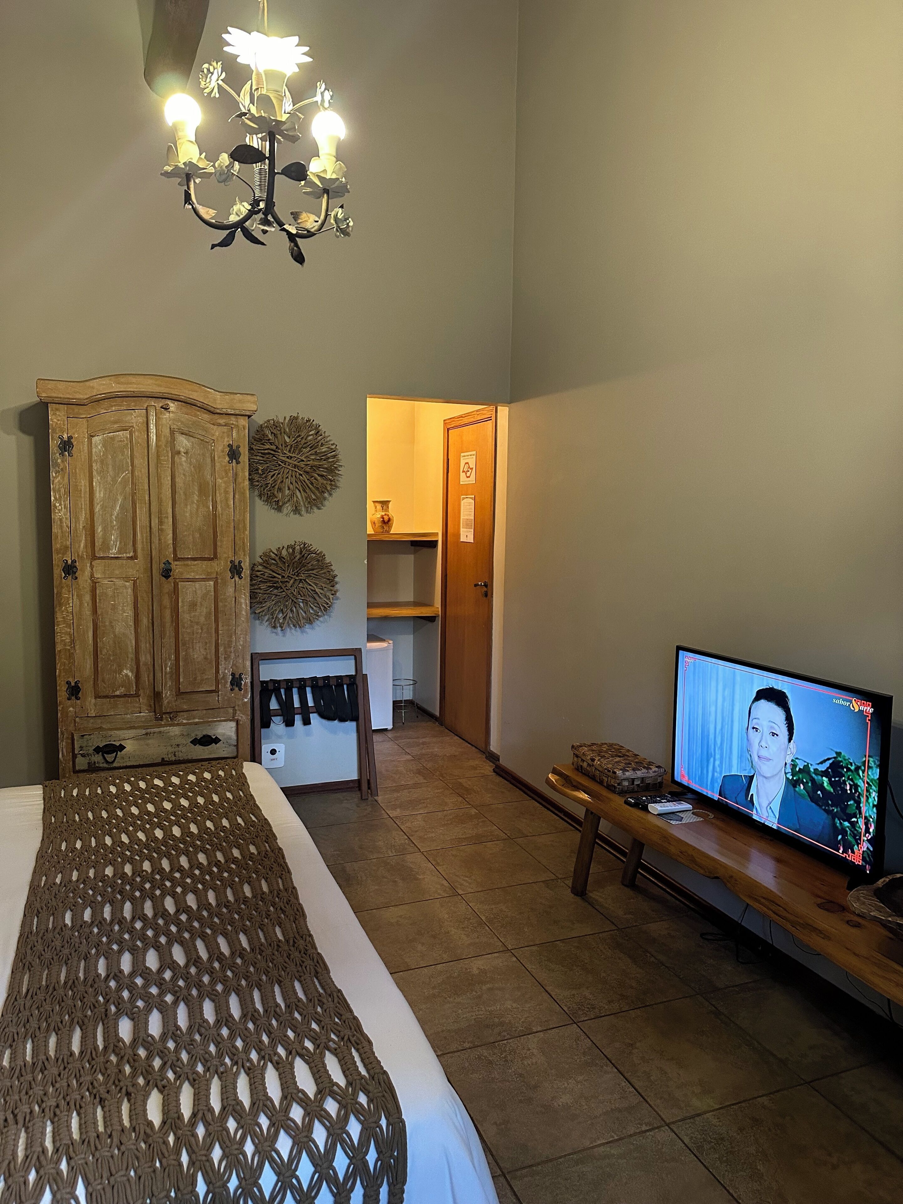 A room with a bed, a wooden wardrobe, a television, and a chandelier.