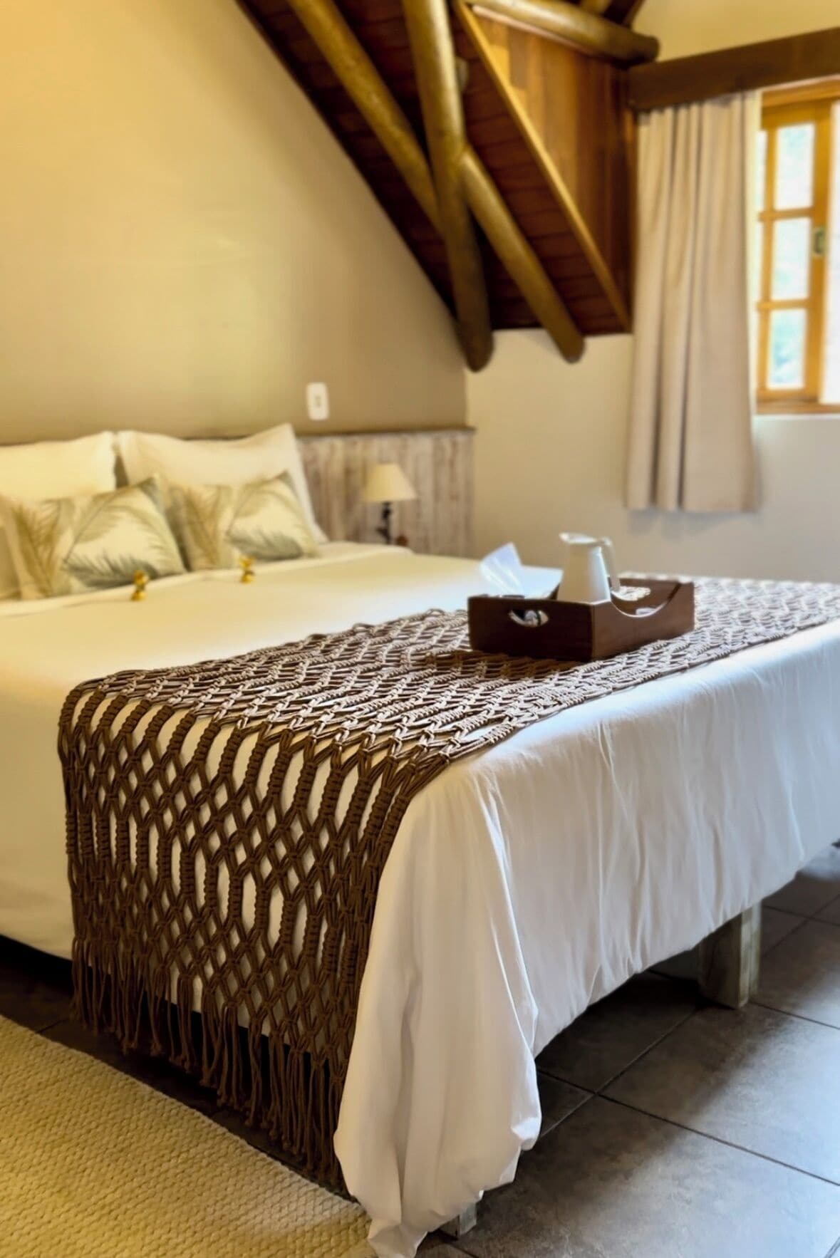 A neatly made bed with a white bedspread and a brown macrame throw.