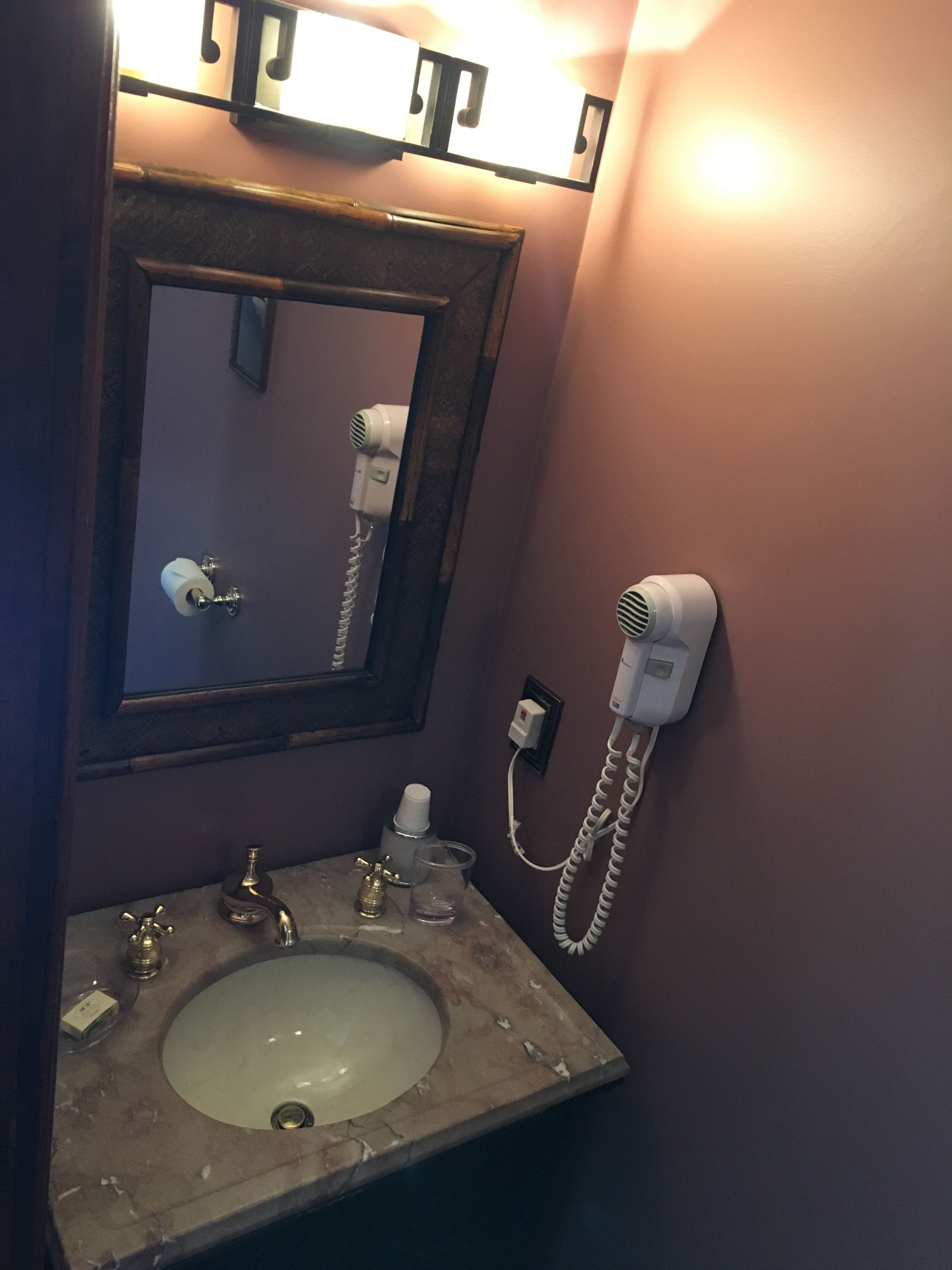 A bathroom with a marble sink, a mirror, a hair dryer, and a towel dispenser.