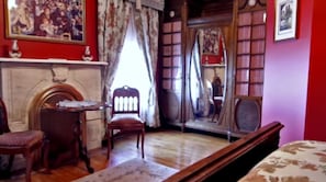 A room with a fireplace, a wooden chair, a table, and a bookshelf. - 1897 Beekman House (Dundee)